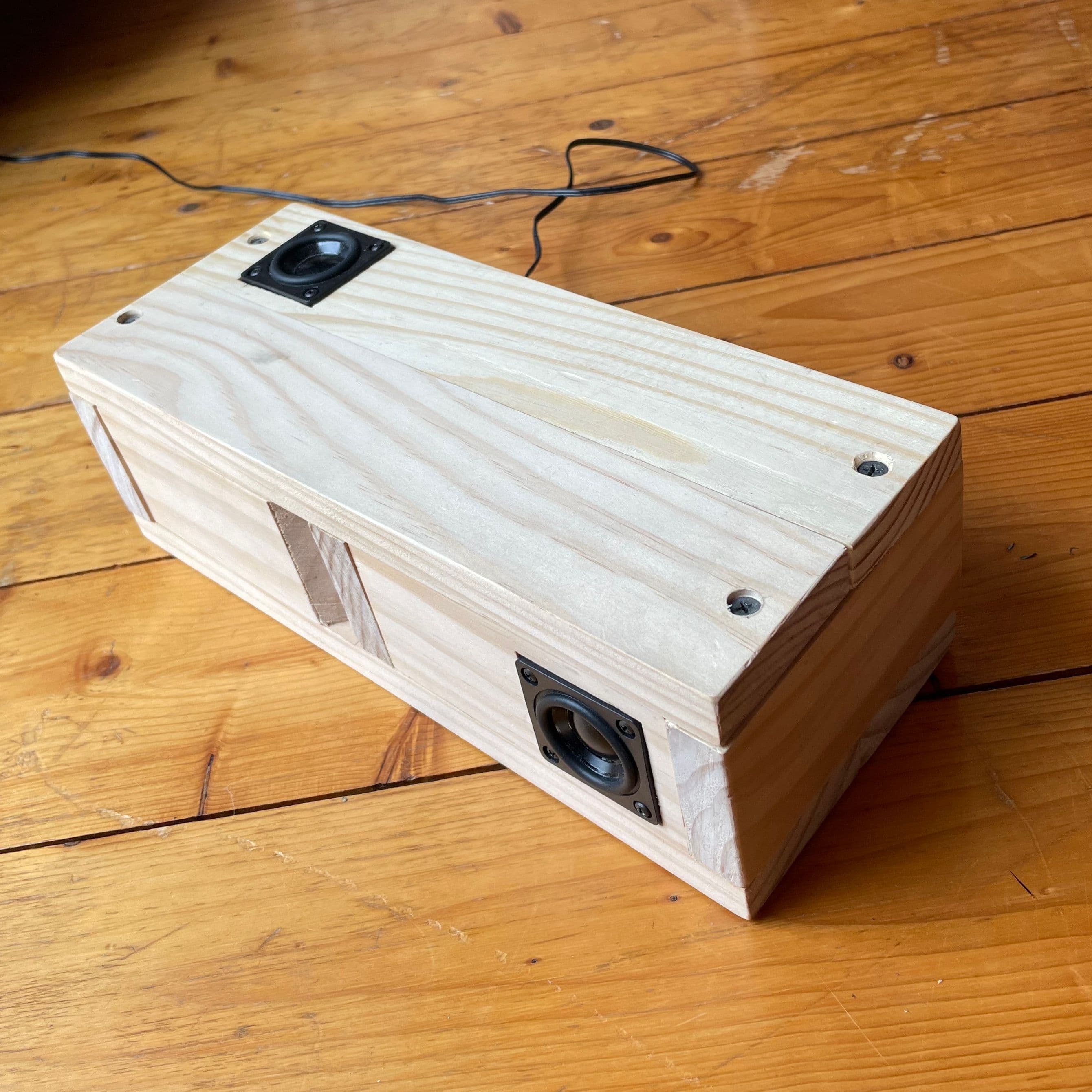 a hand made wooden box on a wooden floor, with two speakers on the top and side