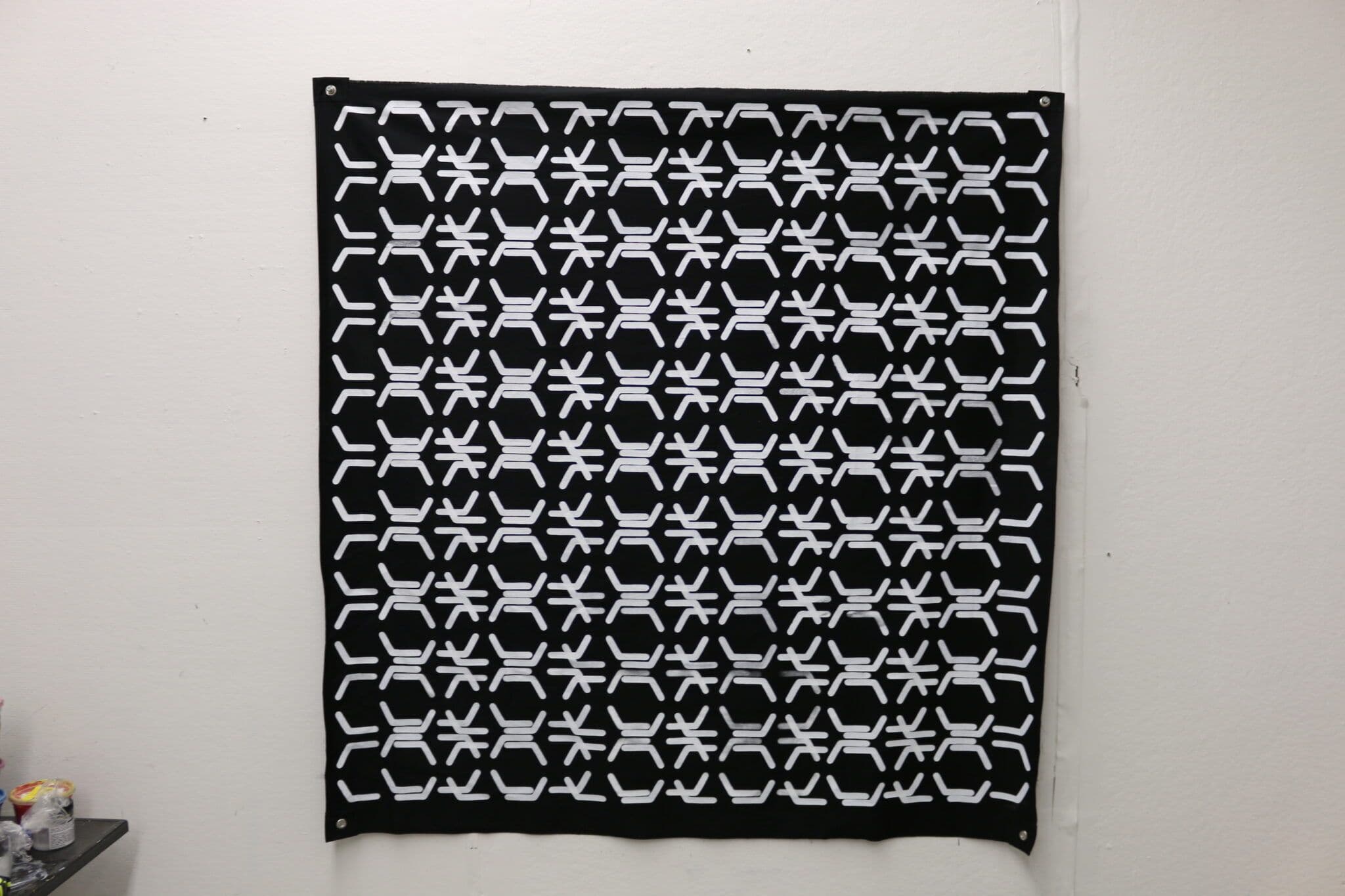 a square canvas piece with grommets in each corner. lines create a shifting pattern