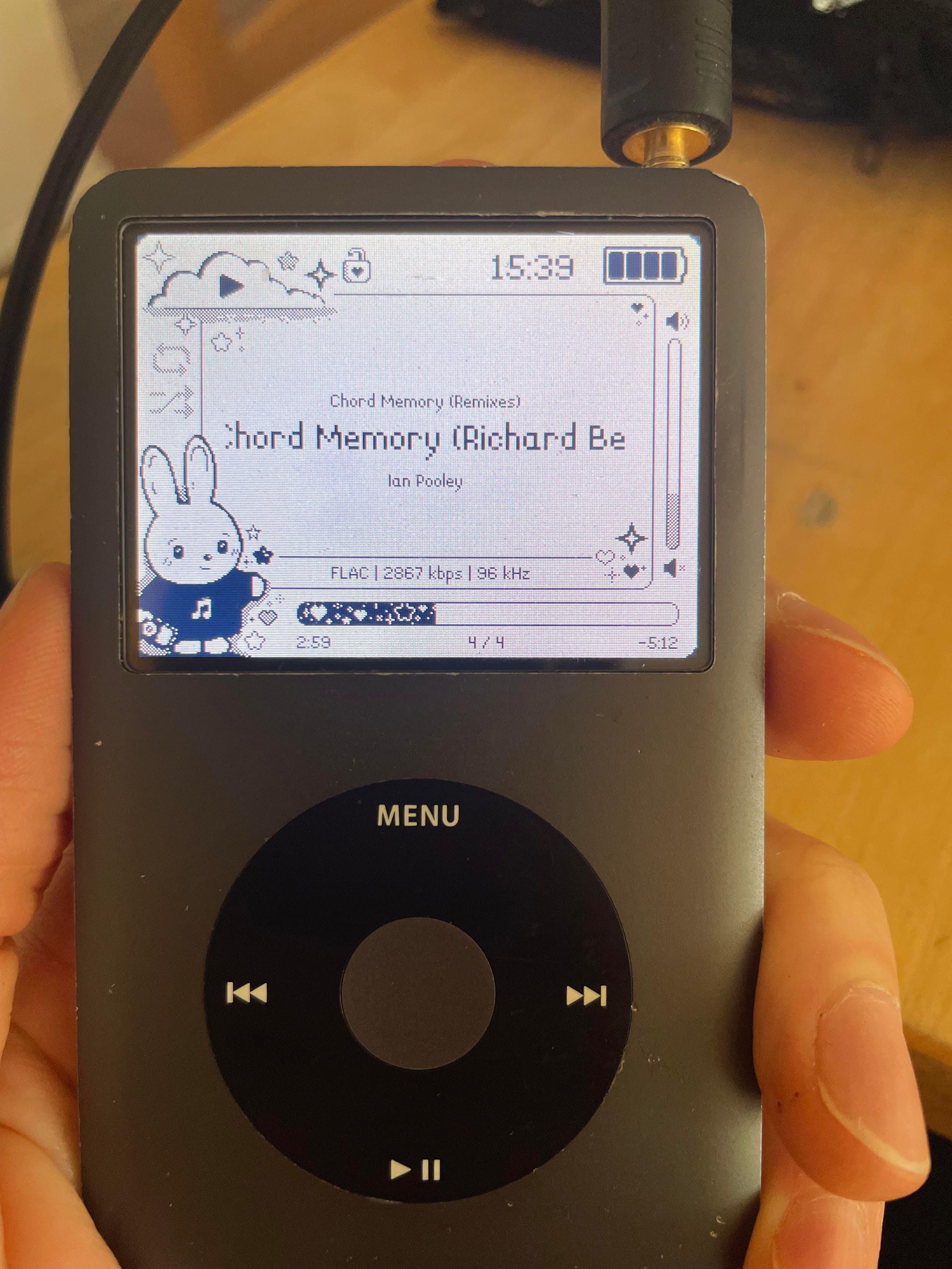 a 7th generation ipod in someones hand. the screen displays the current song playing(Chord Memory(Richard ...) by Ian Pooley. The graphic shows a cute bunny in a sweater.
