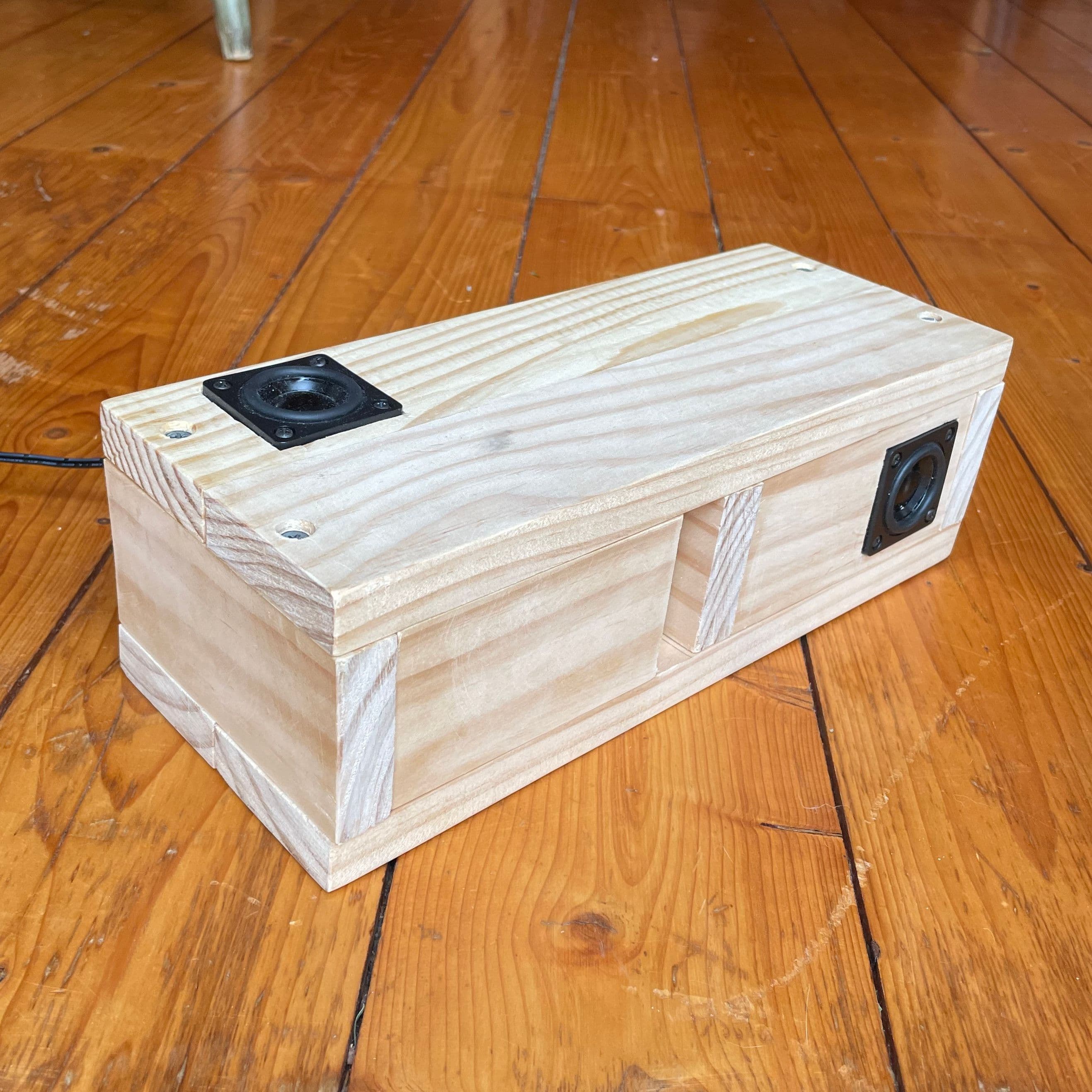 a hand made wooden box on a wooden floor, with two speakers on the top and side